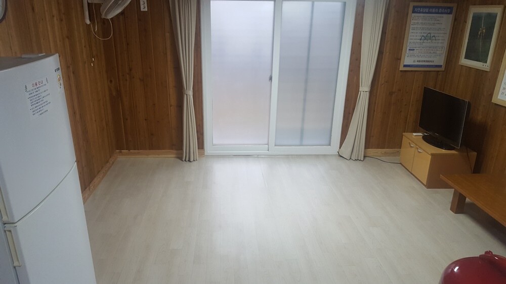제2산림문화휴양관 가래나무의 목재 벽 원룸에 냉장고·TV와 발코니 유리문이 있는 내부