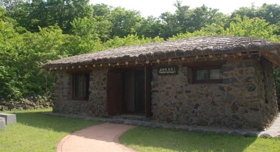숲속의초가 1 상품의 돌담 외벽과 낮은 지붕, 출입구 앞 보행로입니다.