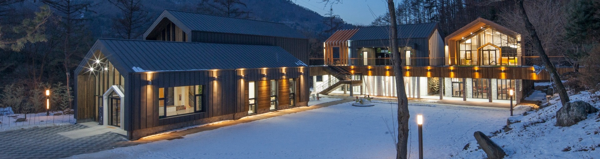 나무와 산비탈 아래 여러 동으로 이어지고 마당에 눈이 놓인 국립유명산자연휴양림 산림복합체험센터